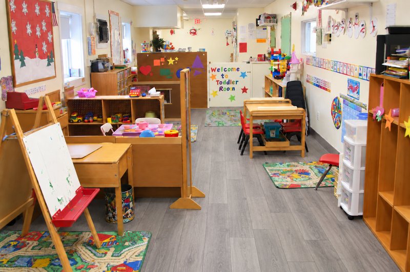 Auburn toddler classroom with child-sized tables, activity shelves, and gray plank flooring leading toward the back